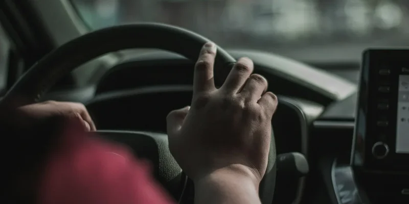 a person driving a car with their hand on the steering wheel