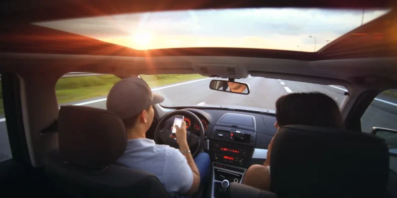 Driver using phone while driving at sunset with passenger in vehicle.